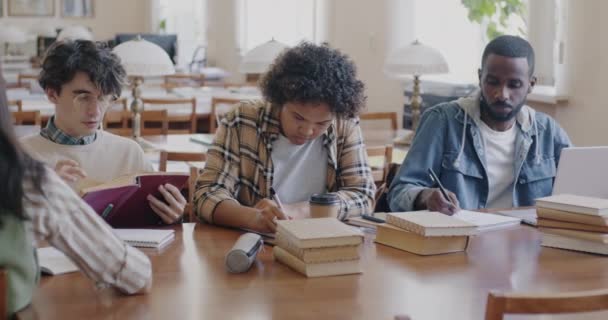 朗らかな若者の大学生が一緒に読み書きをし 図書館の机に座って話をします チームワークと教育の概念 — ストック動画