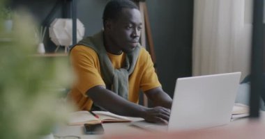 Tired African American man freelancer using laptop then rubbing eyes and face working at home alone. Stress and remote job concept.