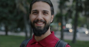 Close-up slow motion portrait of overjoyed Arab man laughing expressing happiness standing in city and looking at camera. People and emotion concept.