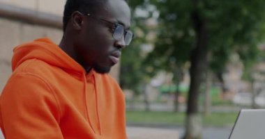 Tilt-down portrait of African American freelancer working with laptop computer typing outdoors in city street. Technology and freelance work concept.