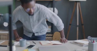 Portrait of young African American man coming to work sitting down at desk and using laptop computer in office. Job and businessperson concept.