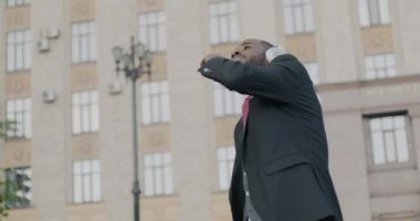 Neşeli öğrenci resmi bir takım elbise giyiyor ve şehirde açık havada dans ederek kulaklıkla müzik dinliyor. Halk ve gençlik kültürü kavramı.