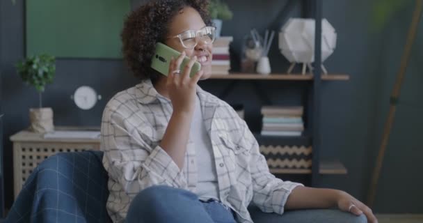 Radosna Afroamerykanka Rozmawiająca Przez Telefon Komórkowy Uśmiechnięta Siedząca Fotelu Mieszkaniu — Wideo stockowe
