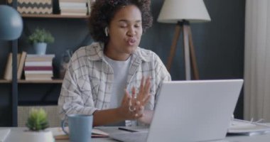 Afrika kökenli Amerikalı bir kadın ofiste kablosuz kulaklık ve dizüstü bilgisayar kullanarak çevrimiçi video görüşmesi yapıyor. Sanal toplantı ve iletişim konsepti.