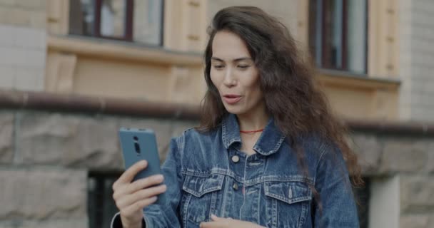 美しいアジアの女性のゆっくりとした動きの肖像画は 市内のスマートフォンを使用してオンラインビデオ通話と手を振ります コミュニケーションとガジェットのコンセプト — ストック動画