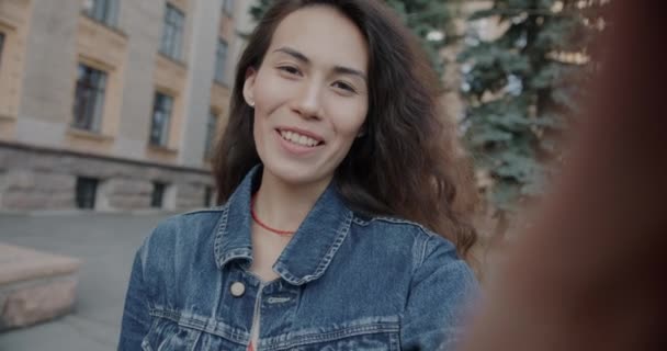 都市の屋外でバーチャルミーティングを楽しむビデオ通話をする幸せな若い女性のゆっくりとした動きの肖像画 アジアの女性が話すと笑う — ストック動画