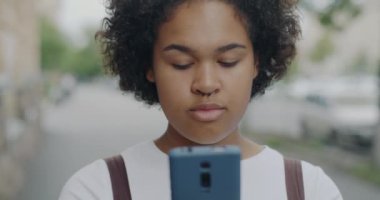 Akıllı telefon ekranına bakıp gülen çekici Afro-Amerikan kız şehirde internet iletişiminin tadını çıkarıyor. İnsanlar ve modern aygıtlar kavramı.