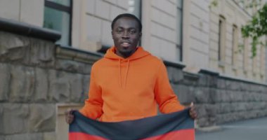 Vatansever Afro-Amerikan bir adamın Alman ulusal bayrağını sallayarak şehirde gülümsemesinin ağır çekimde portresi. Vatanseverlik ve milliyet kavramı.
