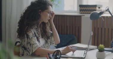 Diz üstü bilgisayar kullanan ve not defterine bilgi yazan bir kız öğrenci. Daireden internet üzerinden çalışıyor. Uzak eğitim ve teknoloji kavramı.