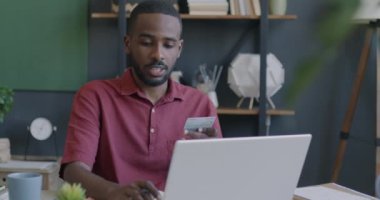 Genç Afro-Amerikalı iş adamı kredi kartı ve dizüstü bilgisayar kullanarak ofisinde mutluluğunu ifade ediyor. Finans ve iş konsepti.
