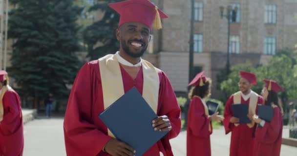 Mezuniyet Mantolu Şapkalı Diplomalı Kameraya Bakıp Gülümseyen Başarılı Afrikalı Amerikalı — Stok video
