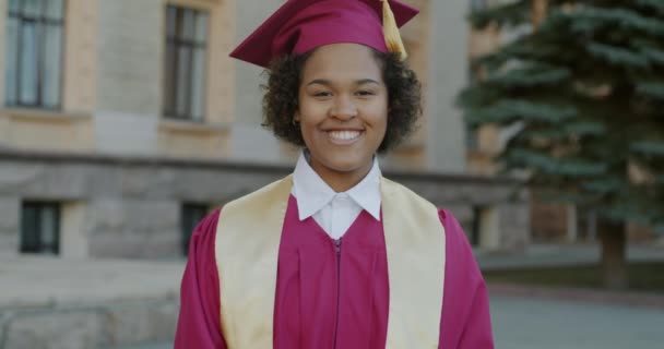 身着毕业帽和长袍的快乐的非洲裔美国女性在大学校园里的慢动作肖像 人与教育概念 — 图库视频影像