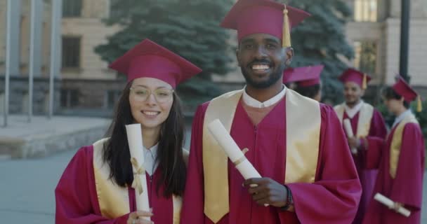 Fröhliche Absolventen Stehen Kleid Und Hut Auf Dem Campus Und — Stockvideo