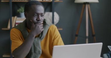 Düşünceli Afro-Amerikalı bir adam laptopla çalışıyor ve görevdeki zor görevleri düşünüyor. Bilgisayar ve çalışan kavramı.