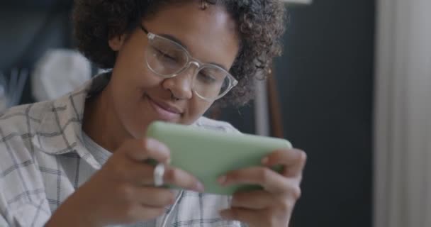 屋内で幸せを表現するスマートフォン勝利とビデオゲームをプレイする楽しいアフリカ系アメリカ人の少女 モバイルエンターテインメントとゲームコンセプト — ストック動画