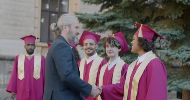 大学教授的慢动作 在毕业典礼上 向各种各样的学生表示祝贺 并握手拥抱在校园里 成熟的男人为年轻人感到高兴 — 图库视频影像