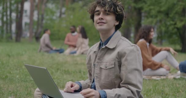 Медленный Портрет Улыбающегося Молодого Человека Сидящего Лужайке Парке Держащего Ноутбук — стоковое видео