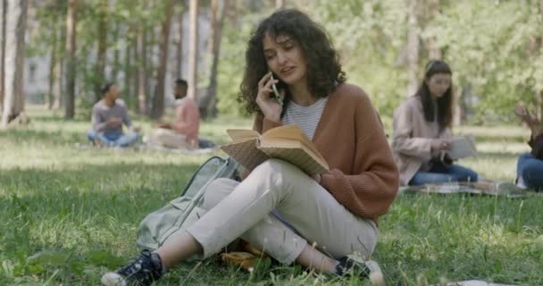 Портрет Радостной Девочки Студентки Читающей Книгу Разговаривающей Мобильному Телефону Сидящей — стоковое видео