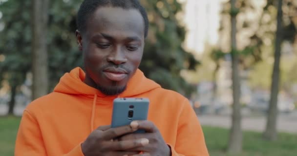 街の外に立っているスマートフォンとのソーシャルメディアコミュニケーションを楽しむ陽気なアフリカ系アメリカ人の肖像画 人とガジェットのコンセプト — ストック動画