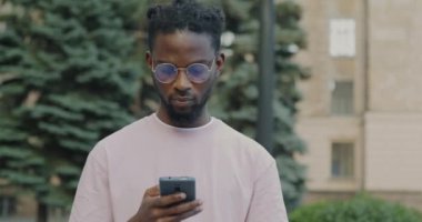 Akıllı telefon kullanan Afro-Amerikalı adamın portresi. Açık havada ekranda iletişim kuruyor. Modern teknoloji ve gençlik kavramı.