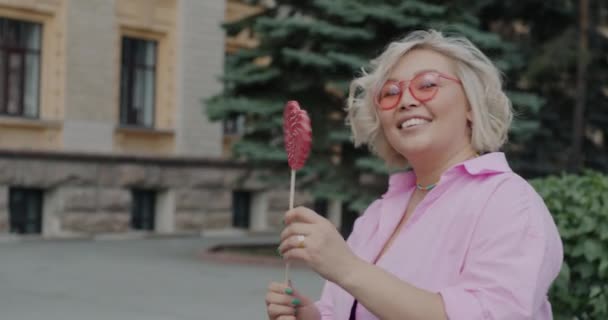 Portret Azjatki Tańczącej Lizakiem Kształcie Serca Noszącej Różowe Okulary Przeciwsłoneczne — Wideo stockowe