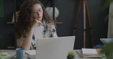 Dizüstü bilgisayarla çalışan düşünceli genç bir kadın evdeki masada oturan iş fikirlerini düşünüyor. Uzak meslek ve modern teknoloji konsepti.