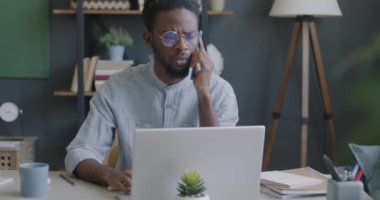 Cep telefonuyla konuşan Afro-Amerikalı bir adam ve ofiste çalışan dizüstü bilgisayardaki bilgileri kontrol ediyor. İş iletişimi ve insan kavramı.