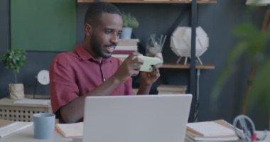 Afrikalı Amerikalı iş adamı akıllı telefonuyla online video oyunu oynuyor ofiste eğleniyor. Oyun aygıtı ve elektronik konsept.