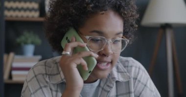 Dost canlısı Afro-Amerikalı kadının cep telefonuyla konuşan ve masada dizüstü bilgisayar kullanan portresi. İş iletişimi ve ofis işi kavramı.