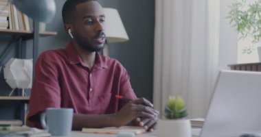 Erkek ofis çalışanı online video görüşmesi sırasında bilgisayar ve kablosuz kulaklık kullanarak iş yazmayı tartışıyor. İş ve sanal buluşma kavramı.