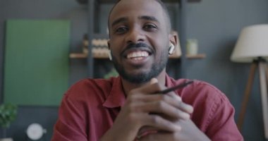 Kulaklıklı, internetten konuşan ve ofisinde el kol hareketi yapan dost canlısı Afrikalı Amerikalı adamın portresi. İş iletişimi ve aygıtlar kavramı.