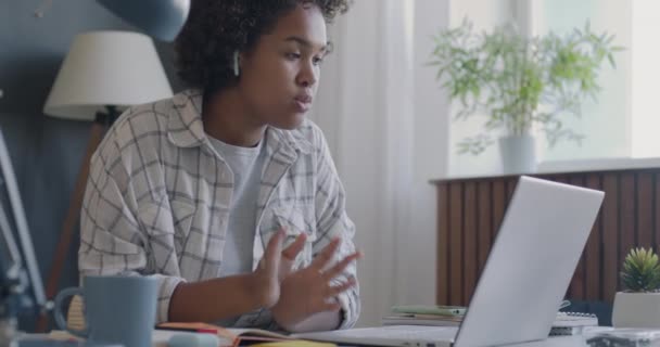 アフリカ系アメリカ人の学生は オンラインビデオ通話中にオンラインで話し 自宅の机でノートブックに書き込みます 遠隔教育とEラーニングのコンセプト — ストック動画