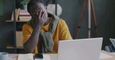 Laptopla çalışan yorgun ve genç bir Afro-Amerikan adam evde yüzlerine dokunarak stres hissediyor. İnsanlar ve aşırı çalışma kavramı.