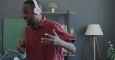 Ofiste dans eden, iş yerinde eğlenen, kulaklık takan neşeli genç bir çalışan. Afro-Amerikalı adam rahatlıyor ve iş başarısını kutluyor.