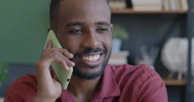 Cep telefonuyla konuşan ve bilgisayarla ofiste çalışan Afro-Amerikalı bir adamın eğik portresi. İş bağlantısı ve teknoloji kavramı.