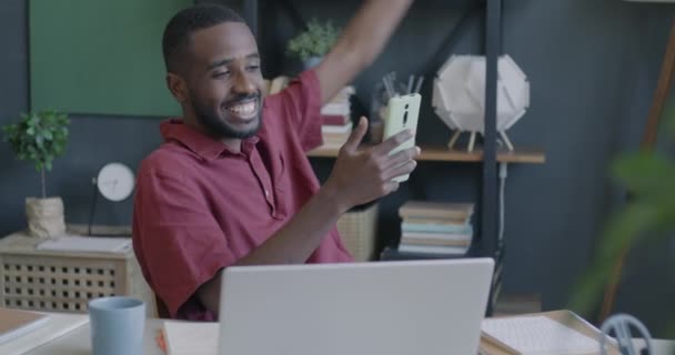 オフィスのスマートフォンカメラを使用してオンラインビデオ通話をする幸せなアフリカ系アメリカ人の従業員 ビジネスマンとバーチャルミーティングのコンセプト — ストック動画
