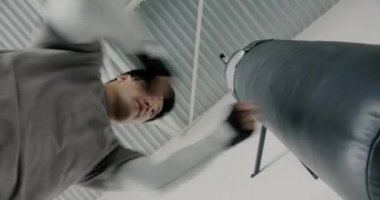 Spor salonunda güçlü bir Asyalı adamın kum torbasına vurduğu düşük açılı atış egzersize odaklanmış. Aktif yaşam stye ve vücut geliştirme kavramı.