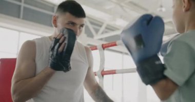 Çocuk savunması hareketleri öğreten boks eğitmeninin ringde eldiven takan bir çocukla konuşması. Spor eğitimi ve sağlıklı çocukluk kavramı.