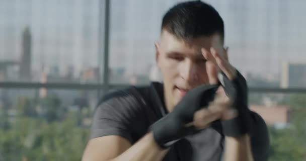 ハンサムなスポーツマンのトレーニングボクシングのスローモーション肖像画は 手を包んでカメラを見ながらジムでパンチ空気を移動します 人とスポーツのコンセプト — ストック動画