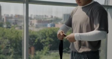 Erkek MMA dövüşçüsü, modaya uygun kıyafetler giyen koruyucu kayışlarla elleri sarma antrenmanına hazırlanıyor. Modern gençlik ve spor konsepti.