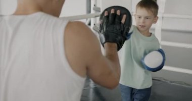 Spor salonundaki yumruklara odaklanmış eldiven giyen boksör eğitmeniyle aktif çocuk eğitimi. Sağlıklı çocukluk ve spor eğitimi kavramı.