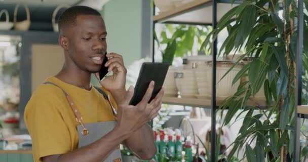 非裔美国人花店的工作人员在手机上与客户交谈 并与绿色植物一起在商店里观看平板电脑屏幕 人与商业概念 — 图库视频影像