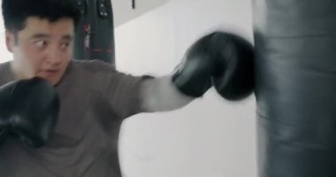 Kum torbasıyla güçlü bir Asyalı adamın antrenmanının ağır çekimde spor salonunda boks eldivenleriyle onu yenmesi. Aktif yaşam tarzı ve spor konsepti.