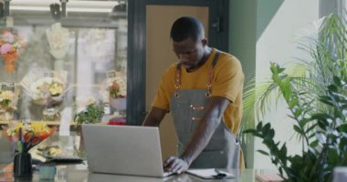 Çiçekçi müdürü dizüstü bilgisayar kullanıyor ve bitki taşıyan genç bir bayanla konuşuyor. Çiçekçilik ve perakende konsepti.