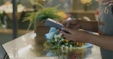 Yakın plan NFC terminali ve çiçekçi müşterisi cep telefonu alımıyla ödeme yapıyor. Alışveriş ve para kavramı.