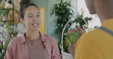 Memnun müşteri Orta Doğulu kadın çiçekçi dükkanında çiçeklenme hakkında tezgahtarla konuşuyor. Perakende ve iletişim konsepti.