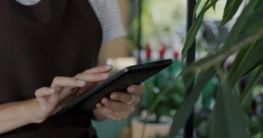 Önlüklü kadın çiçekçide envanter sayımı yaparken kadının tablet dokunmatik ekranla çalışmasını yakından çek. Aygıtlar ve iş konsepti.