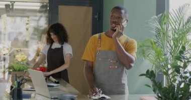Çiçekçi dükkanı müdürü, arka planda çalışan satıcı kadın cep telefonuyla konuşan Afrikalı Amerikalı adam. Halk ve iş kavramı.