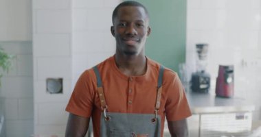 Çekici Afrikalı Amerikalı profesyonel bir baristanın ağır çekimde portresi. Modern kahve evinde önlük giymiş kameraya gülümsüyor.