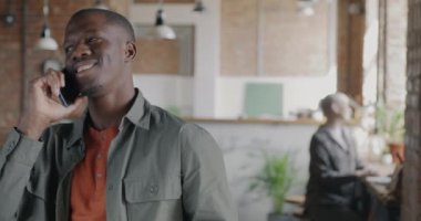 Neşeli Afrikalı Amerikalı adam cep telefonuyla konuşuyor ve iş yerinde kahve içmeye gidiyor. İletişim ve içecek konsepti.